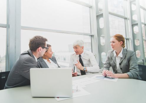 Business team sitting by the table with laptop and documents in office