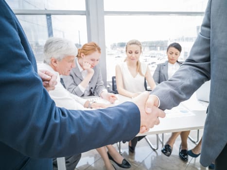 Handshake of business partners after discussion of the financial reports, their team on background