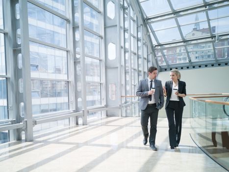 Businessman and businesswoman walk together and talk about business holding coffee in hand