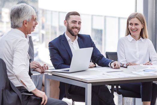 Business people laughing at workplace sitting at conference table with reports. Business meeting and communication concept