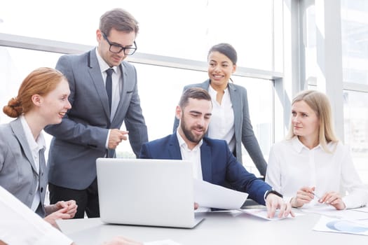 Business team sitting by the table with laptop and documents in office