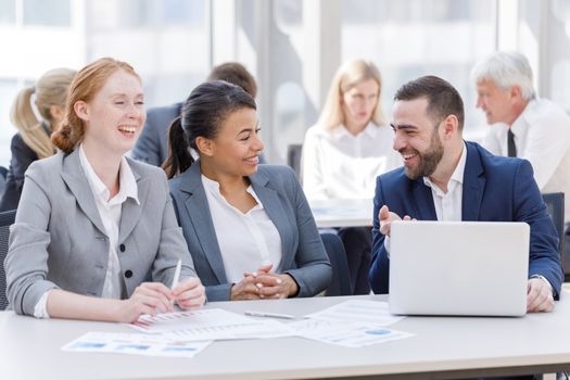 Business team sitting by the table with laptop and documents in office