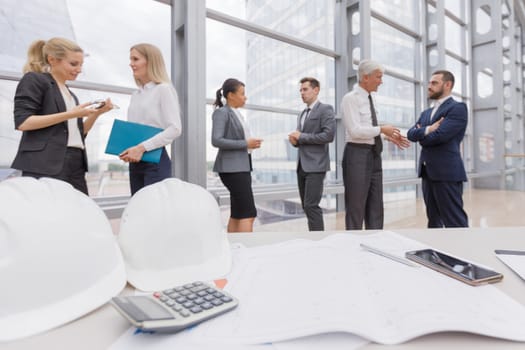 Business people team discuss construction issues , hardhat , blueprint , contract , documents , calculator on office table