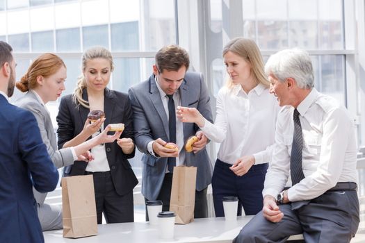 Business people having coffee break eating donuts together in office