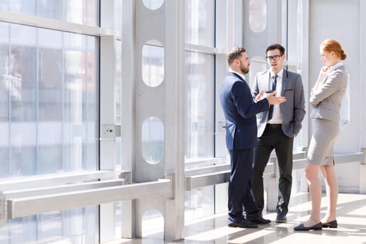 Businessmen and businesswoman talk about business holding coffee in hand at break in office