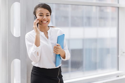 Happy african businesswoman smiling and talking on the phone, holding folder of documents