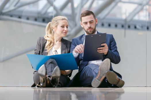 Two business people at break in office sitting on the floor and discuss working documents