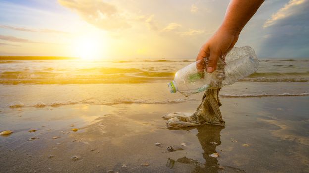 The hand is picking up trash on the beach, the idea of environmental conservation