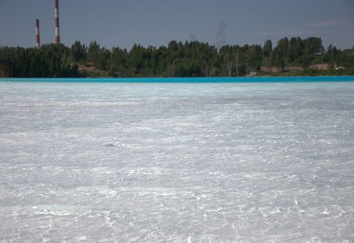 Forest lake with white-blue water, in the background pipes of an old plant.