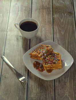 Light dessert, plate with Viennese waffles with icing and topping, a cup of coffee and a fork.