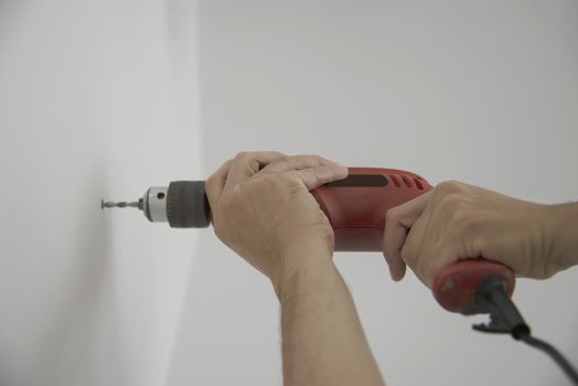 Man using hand drill device for installing home furniture at new white wall - people DIY home furniture installation concept