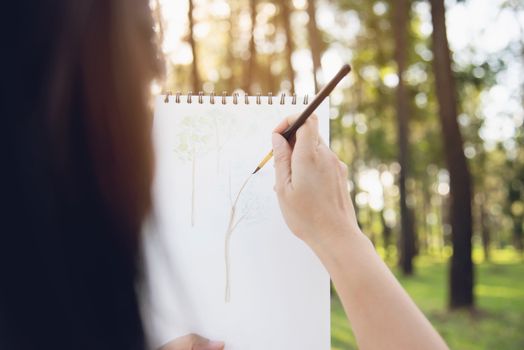 Relax woman painting water colour art work in green garden forest nature - people with creative art in nature stress reduction and meditation concept