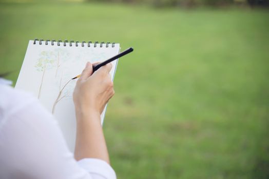 Relax woman painting water colour art work in green garden forest nature - people with creative art in nature stress reduction and meditation concept