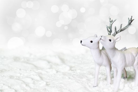 Glimmering white reindeer and roe deer standing in the snow. Winter festive concept with light shiny bokeh background.