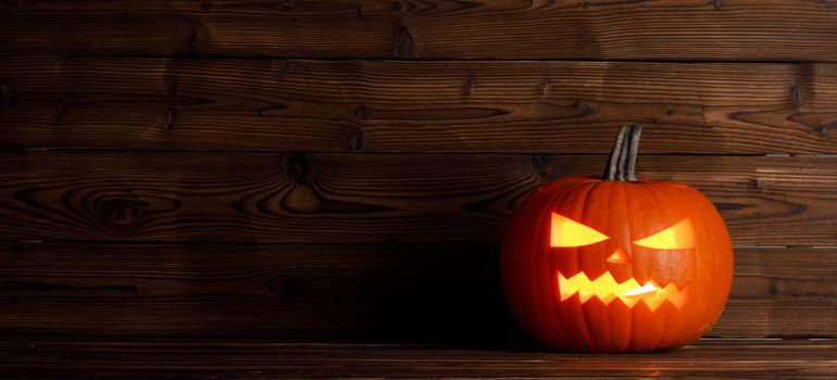 Halloween pumpkin head jack o lantern with candle inside on wooden background