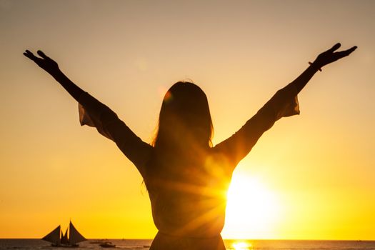 Free happy woman raising arms watching the sun and sea in the background at sunset