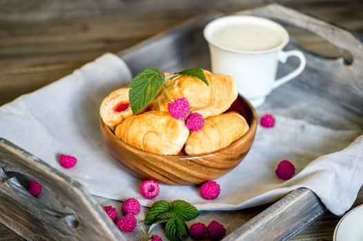 Croissants with raspberries on a wooden tray. The concept of a wholesome breakfast