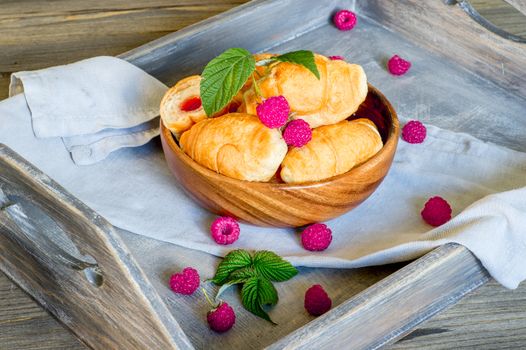 Croissants with raspberries on a wooden tray. The concept of a wholesome breakfast