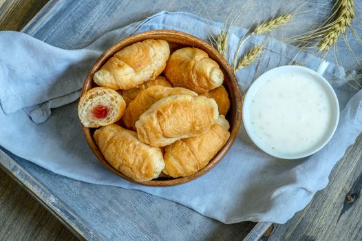 Croissants, a cup with kefir and ears of grain on a wooden tray. The concept of a wholesome breakfast