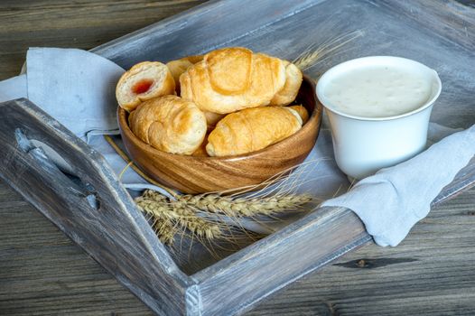 Croissants, a cup with kefir and ears of grain on a wooden tray. The concept of a wholesome breakfast