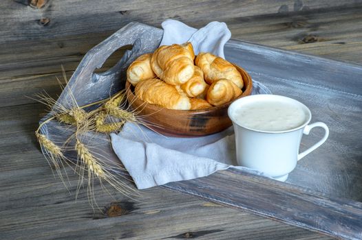 Croissants, a cup with kefir and ears of grain on a wooden tray. The concept of a wholesome breakfast