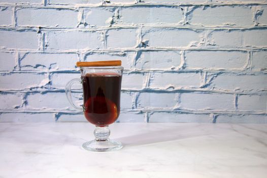 A glass of mulled wine with lemon and a cinnamon stick on top.