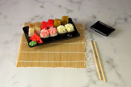 A set of sushi on a bamboo napkin, next to chopsticks and a cup with soy sauce.