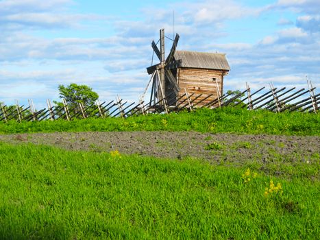 Wooden mill of the last century at the fence of the poles in the summer.
