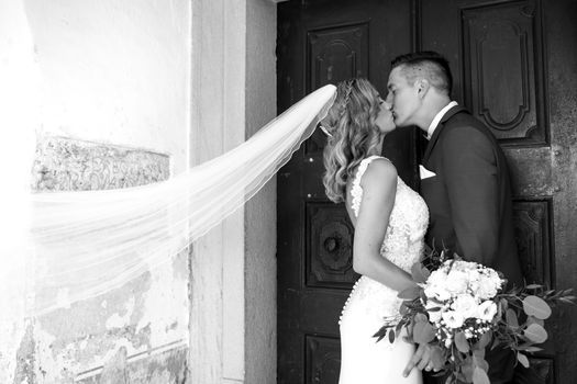 The Kiss. Bride and groom kisses tenderly in front of church portal. Close up portrait of sexy stylish wedding couple kissing. Black and white photo.