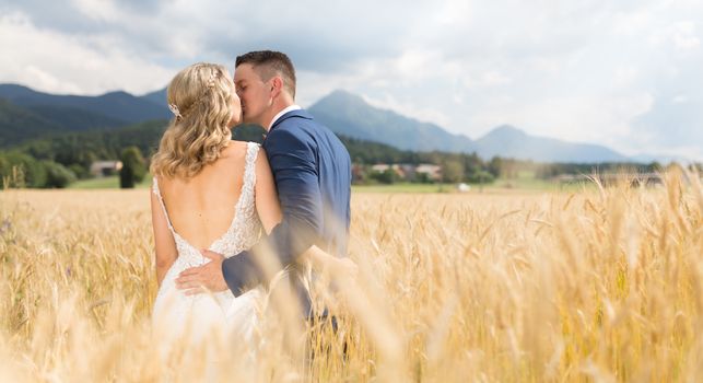 Bride and groom kissing and hugging tenderly in wheat field somewhere in countryside in Slovenian . Caucasian happy romantic young couple celebrating their marriage.