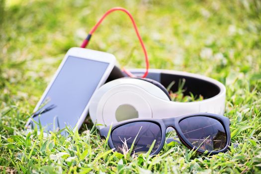 Close-up shot of sunglasses, headphones and smart phone on green grass.