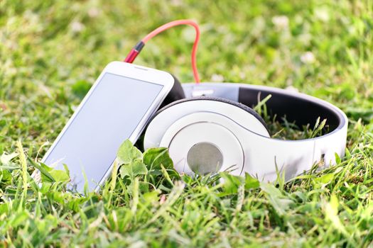 Close-up shot of headphones and a smart phone on green grass, on the meadow.