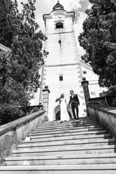 The Kiss. Bride and groom holding hands walking down the staircase in front of a small local church. Stylish wedding couple kissing. Black and white photo.