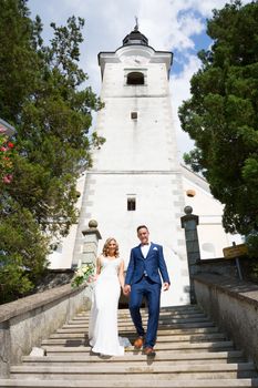 The Kiss. Bride and groom holding hands walking down the staircase in front of a small local church. Stylish wedding couple kissing.