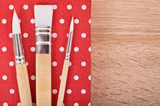 Close up shot of paint brushes on a wooden background.