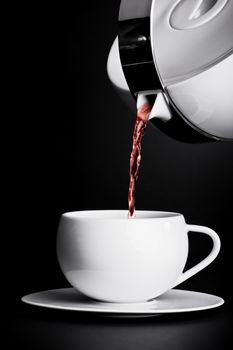 Pouring tea on black background. Low key photograph of a tea pouring in a cup from a tea pot.