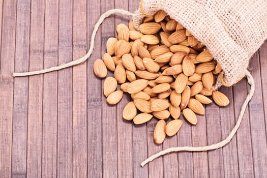 Close up shot of spilled almonds spilled from a burlap sack, on a wooden background.