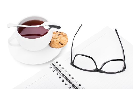 Glasses and notebook with a cup of tea and cookie, isolated on white background.