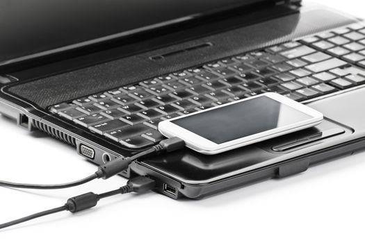 Data transfer between devices. Close up shot of mobile phone connected to a laptop with a usb cable, isolated on white background.