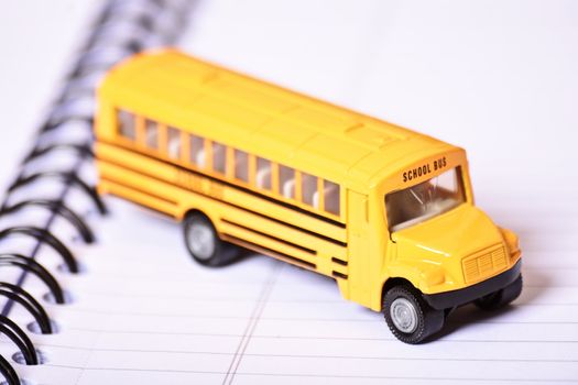 Close up shot of a toy school bus on top of an open spiral notebook. 