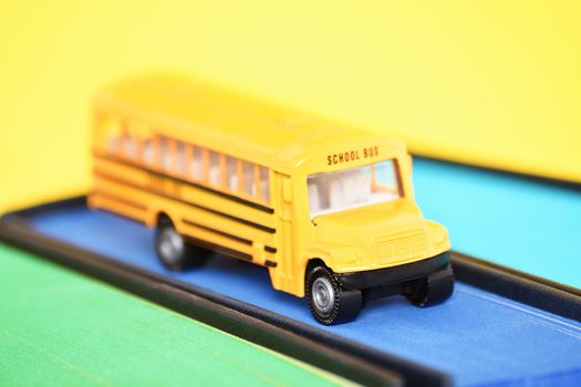 Close up shot of a toy school bus on top of a book with blue sprayed edges on yellow background.