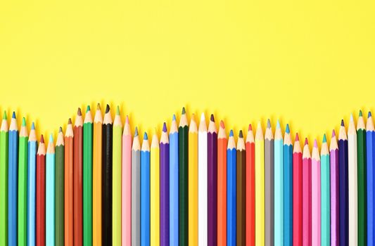 Colorful coloring pencils displayed in a wave on yellow background.