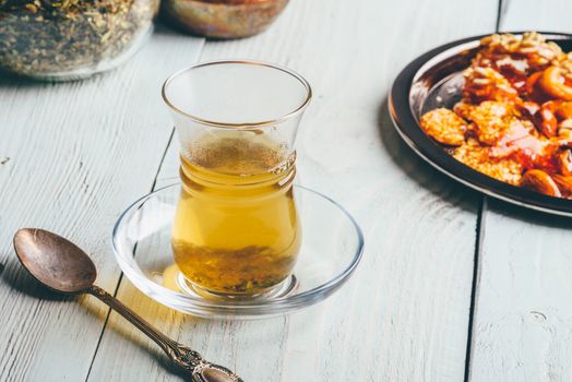 Green tea in armudu glass with oriental nut delights on metal plate over light wooden surface