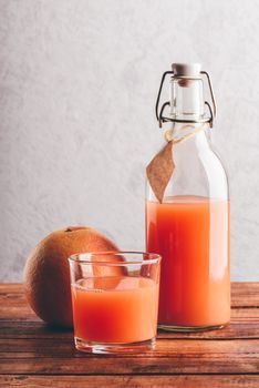 Bottle of grapefruit juice with glass and fruit on wooden surface