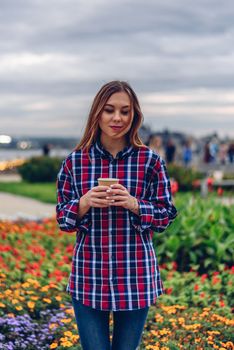 Coffee on the go. Beautiful young woman holding coffee cup and standing in the park