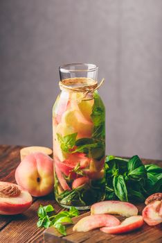 Bottle of Infused Water with Sliced Peach and Basil Leaves. Knife and Ingredients on Cutting Board. Vertical Orientation.