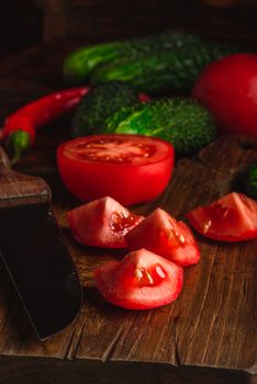 Sliced tomatoes on cutting board and cucumbers with chili peppers over wooden background.