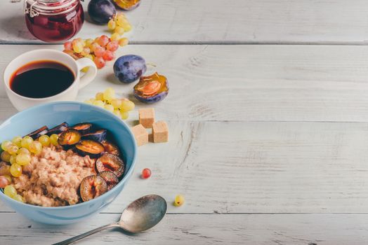 Healthy breakfast concept. Porridge with fresh plum, green grapes and cup of coffee. Ingredients over wooden background.