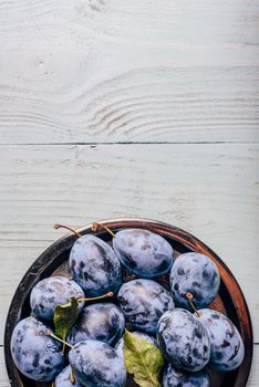 Ripe plums on metal plate over light wooden surface. Copy space