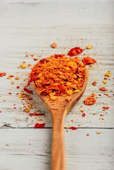 Spoonful of crushed red chili pepper over wooden background